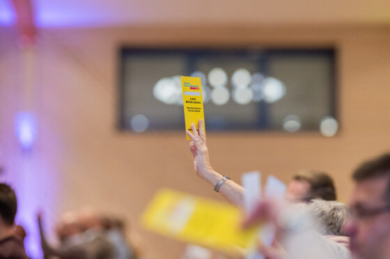 Hand holding yellow voting card in crowd.