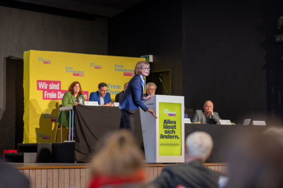 Woman gives speech at FDP event with posters in the background.