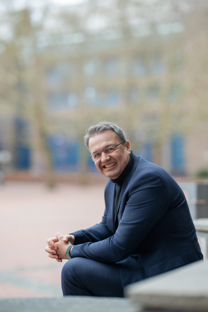 Man in a suit sits outside and smiles.