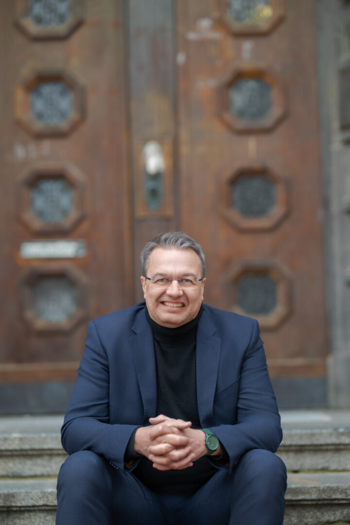 Man sitting on stairs in front of wooden door, smiling friendly.
