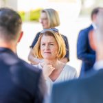 Frau steht im Freien, umgeben von Menschen.