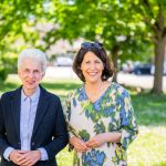 Zwei lächelnde Frauen im Grünen vor Bäumen.