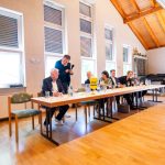 Personen am Konferenztisch mit FDP-Schild in Saal.