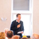Person spricht in Mikrofon bei Versammlung.